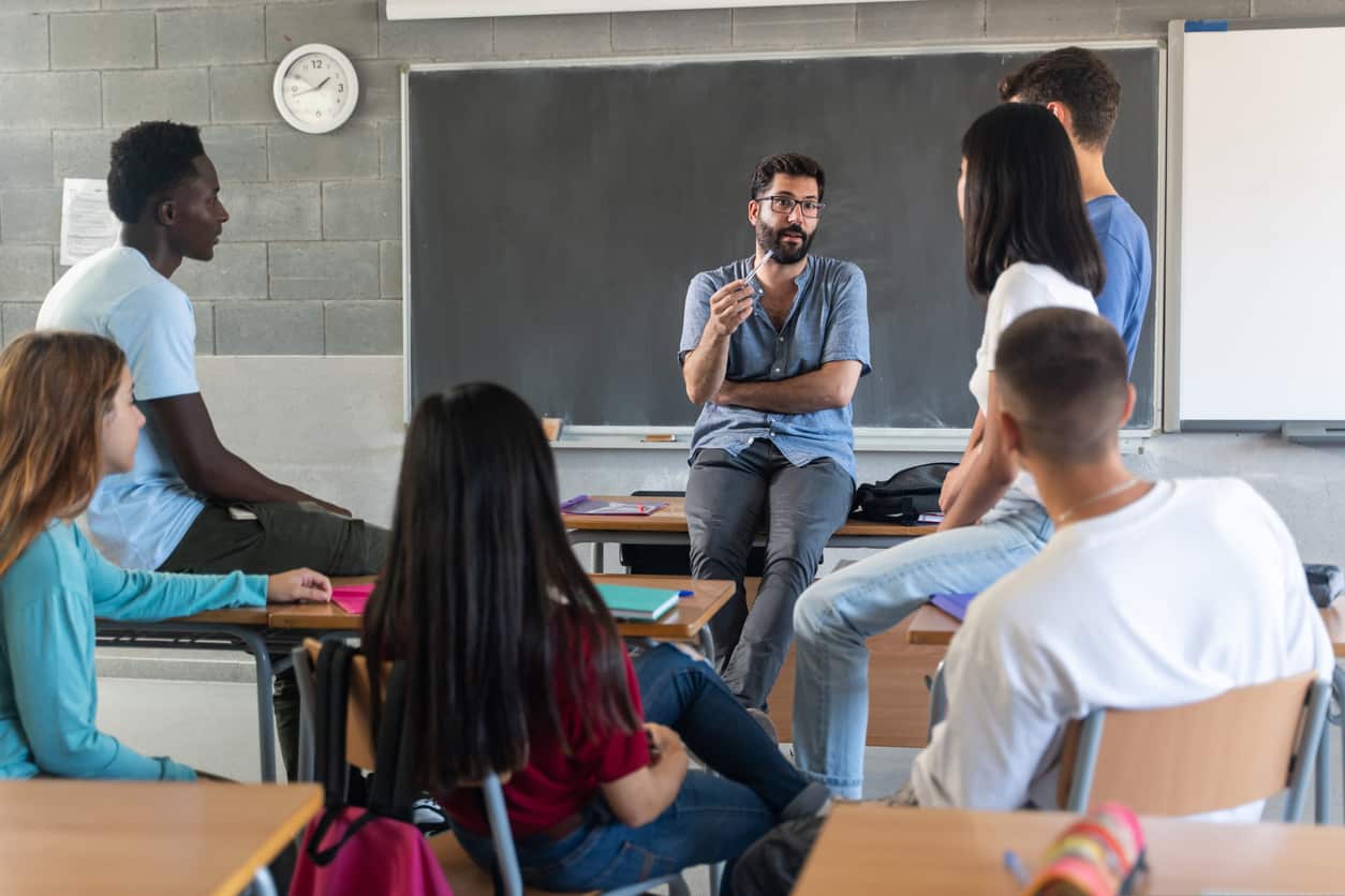 Young teacher talking with teenager students seating in a circle at school.